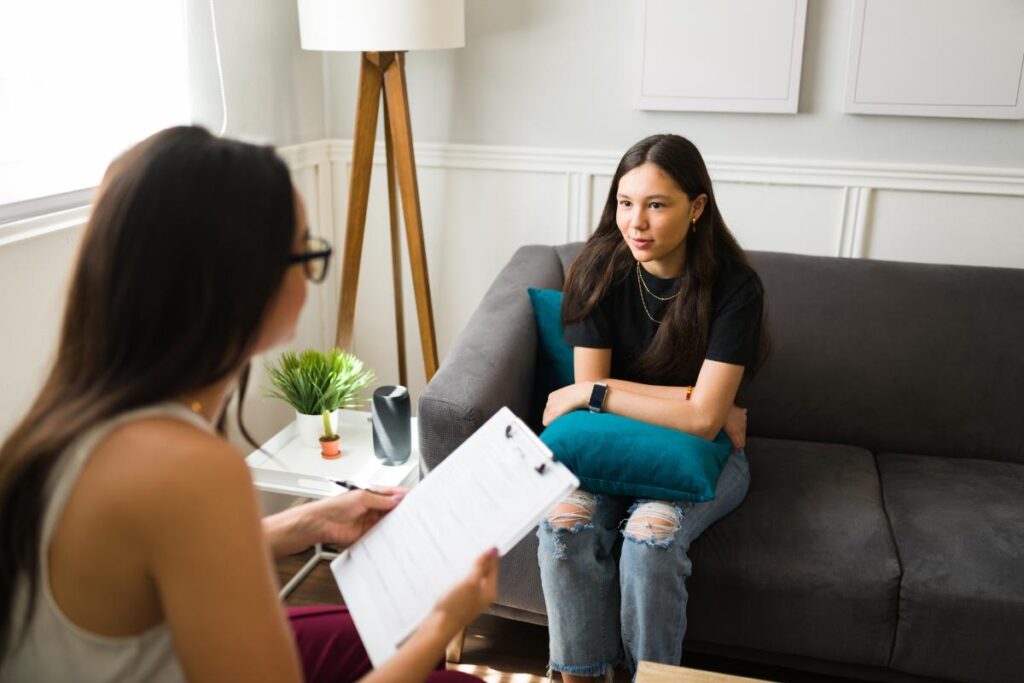 a teen sits on a couch with a therapist during acceptance and commitment therapy for adolescents