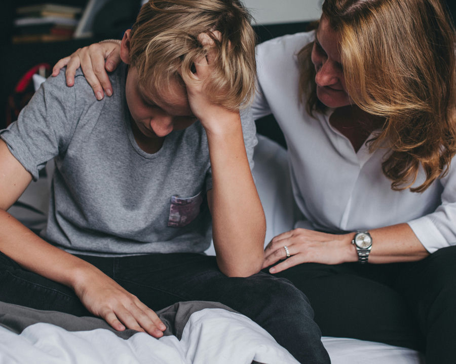 Parent talking with their teenager in a bedroom setting, watching for signs of bullying and emotional distress.