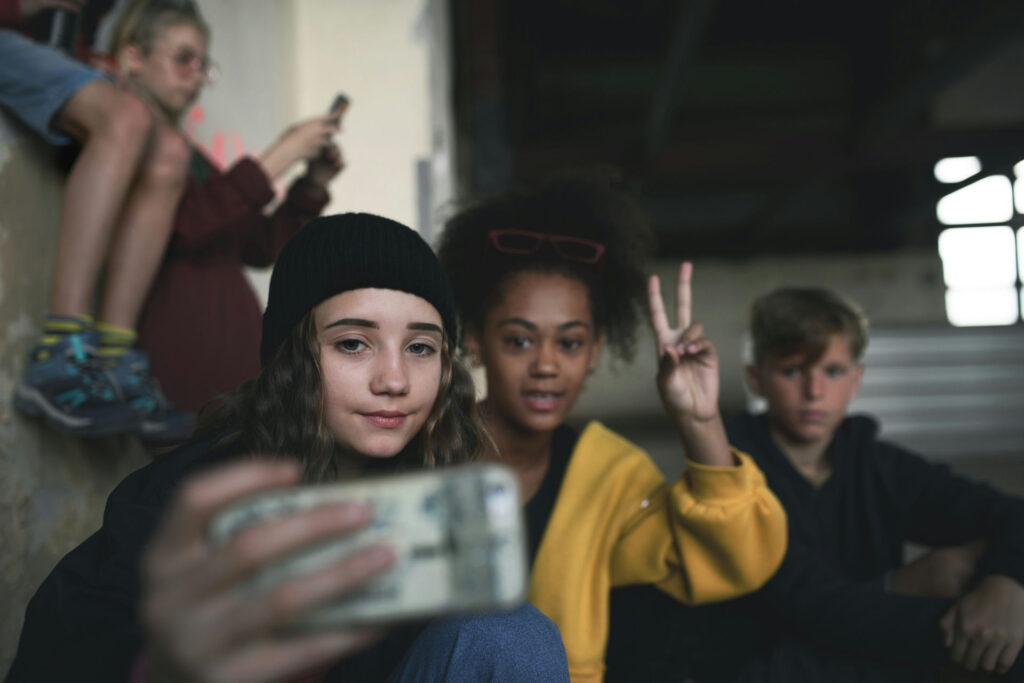 Teen sitting alone in a school hallway while classmates chat nearby, representing bullying and social isolation in adolescence.